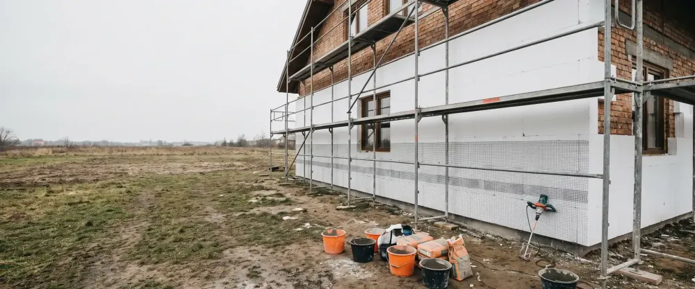 Ściana domu jednorodzinnego obłożona płytami styropianu, rusztowanie wzdłuż elewacji